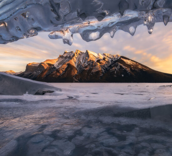 A winter photograph of the Canadian Rockies from Lake Minnewanka in Banff National Park from an ice cave at sunset